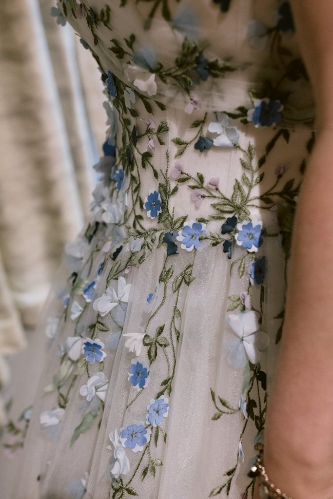 Close-up of a person wearing a white dress with blue and purple floral embroidery and green vine details, perfect for a Late Summer Wedding at The Maynard near Padley Gorge.