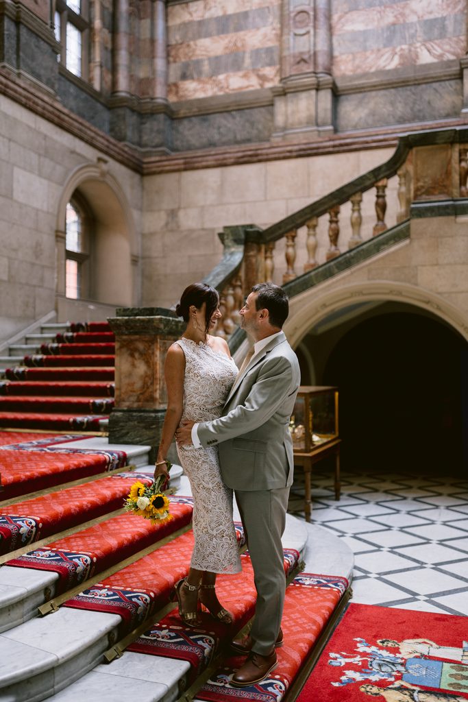 A bride in a white lace dress with a sunflower bouquet and a groom in a light suit stand together on a red-carpeted staircase at a Sheffield Town Hall wedding.