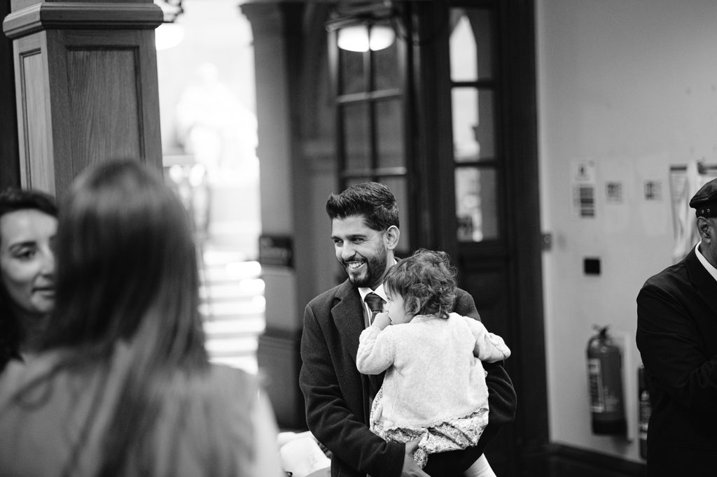 A smiling man in a suit jacket holding a toddler during an intimate Sheffield wedding.
