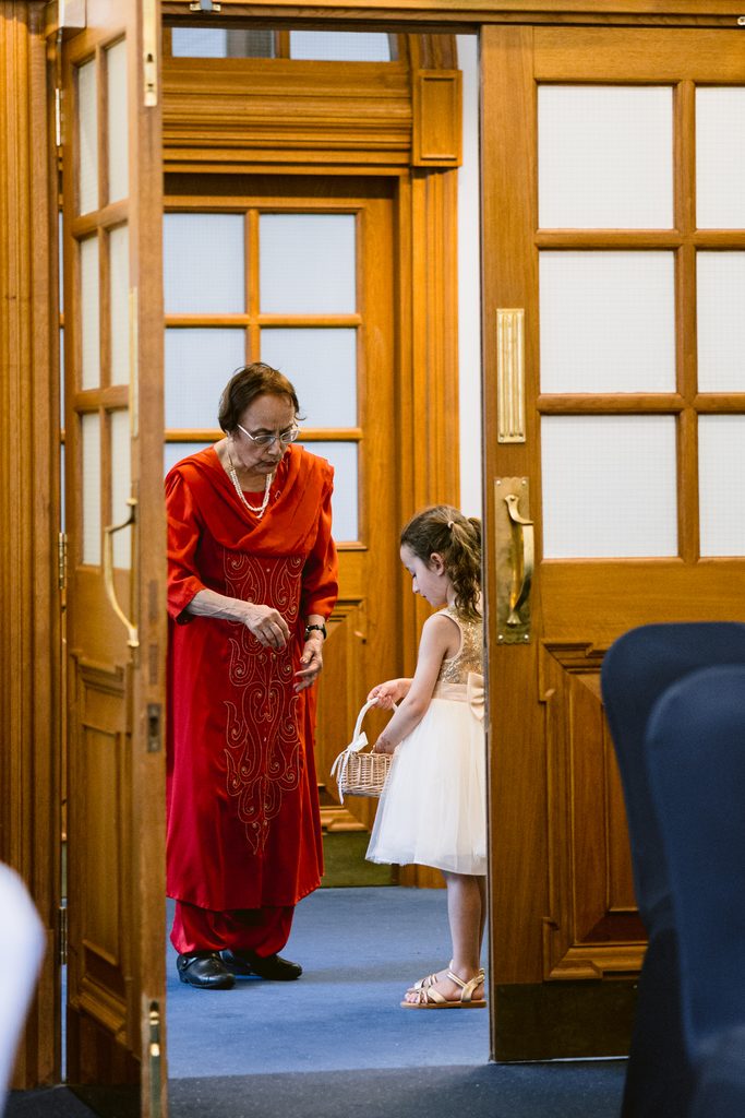 An elderly woman in a red tunic and a young girl in a white dress stand in a doorway at an intimate Sheffield Town Hall wedding.