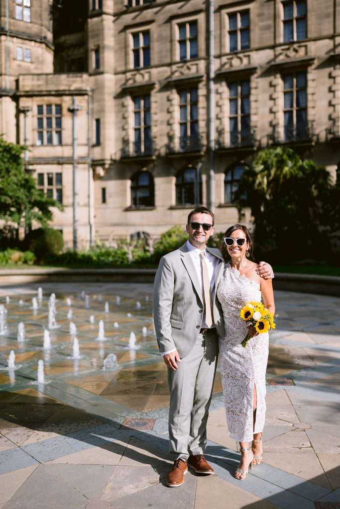 A couple pose for an intimate wedding photo in front of the Sheffield Town Hall and a water fountain.