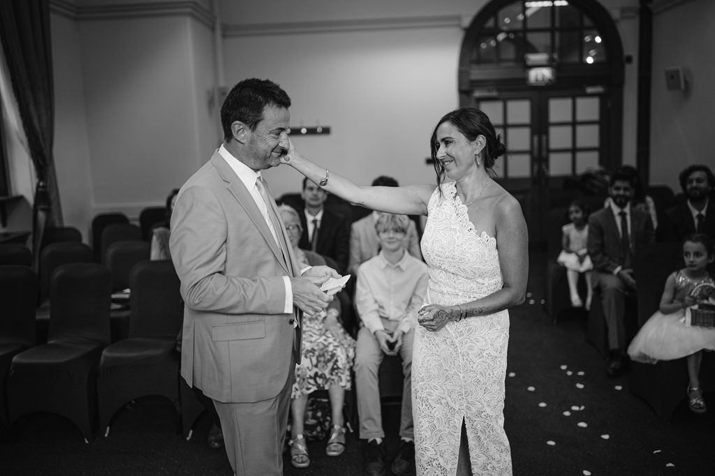 A woman in a white lace wedding dress touches the face of a man in a light suit during an intimate Sheffield wedding ceremony.