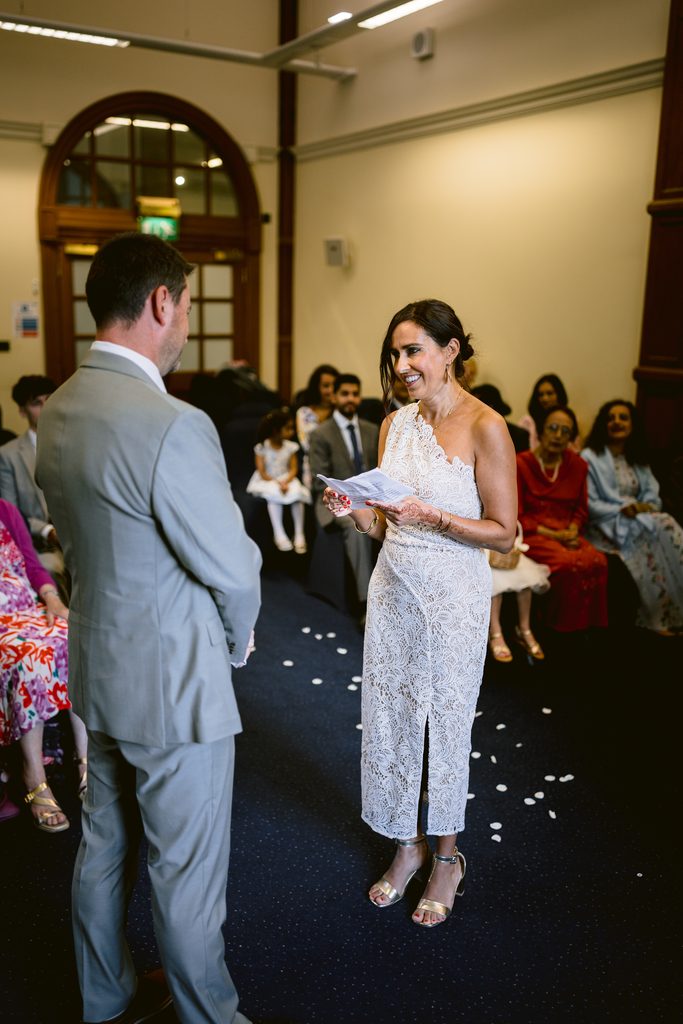 A bride in a white lace dress reads vows to a groom in a grey suit during an intimate Sheffield Town Hall wedding.