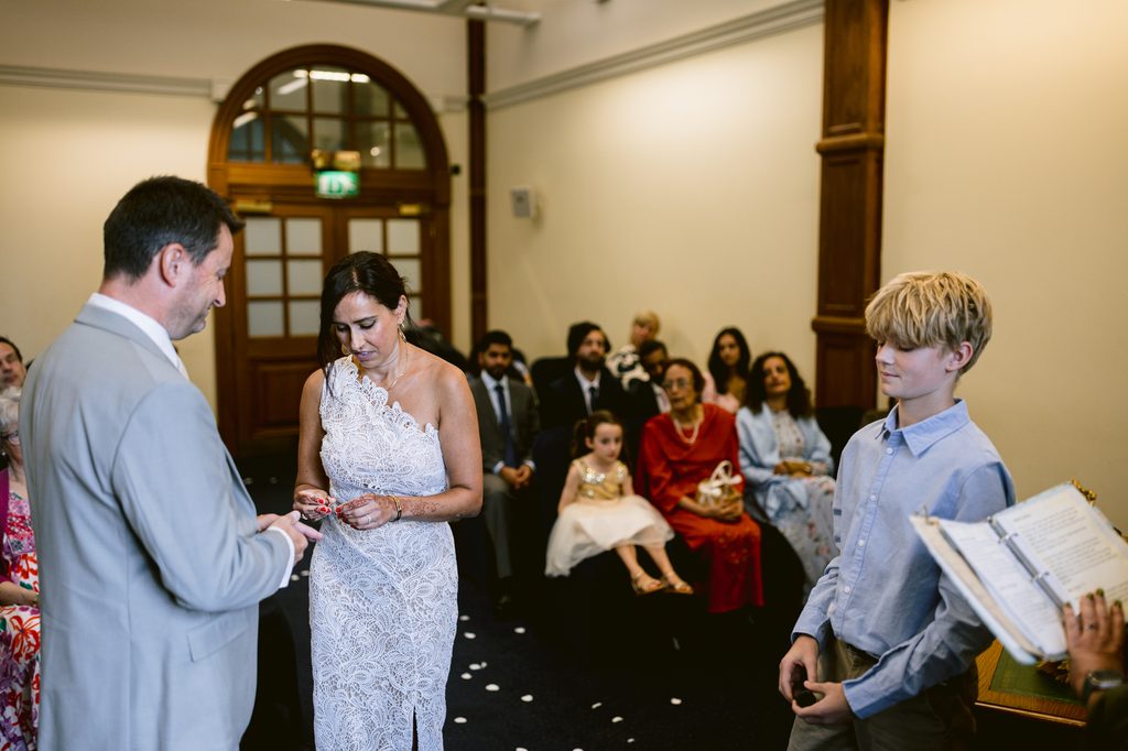 A man and woman stand during an intimate wedding ceremony at Sheffield Town Hall, with a young boy standing nearby and guests seated in the background.