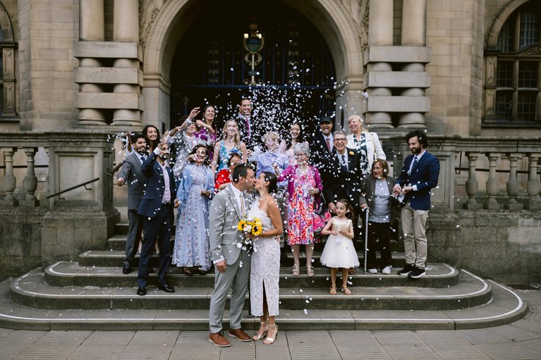 A newlywed couple snogs on the stone steps of Sheffield Town Hall as guests shower them with confetti.
