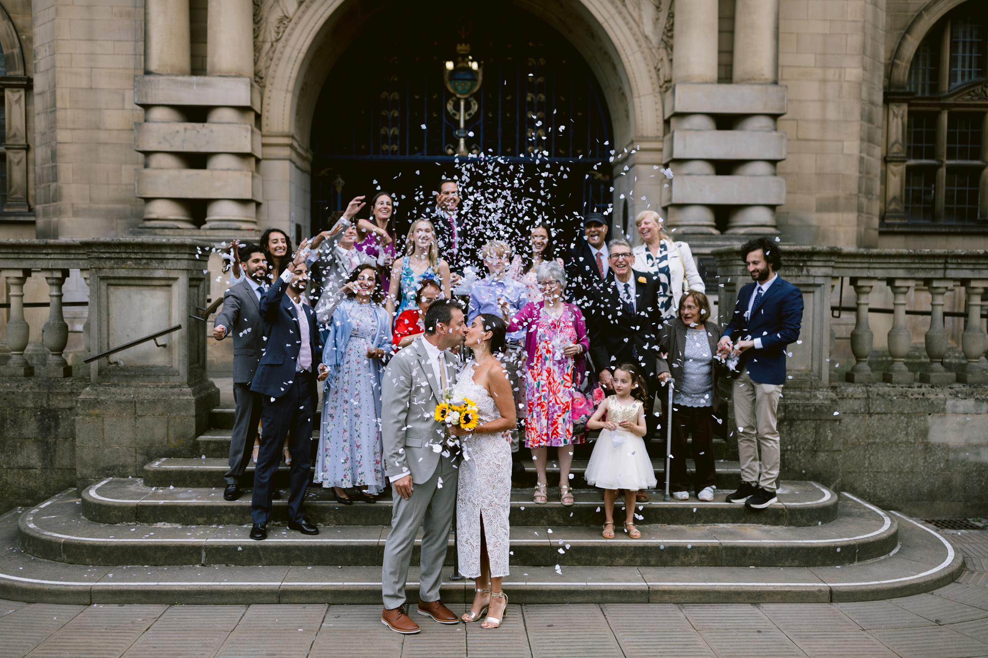A newlywed couple snogs on the stone steps of Sheffield Town Hall as guests shower them with confetti.