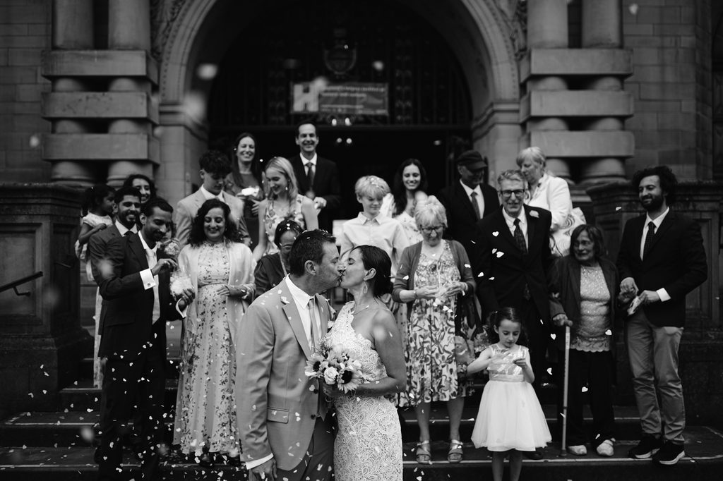 A bride and groom kiss as guests throw confetti on the steps of Sheffield Town Hall during an intimate wedding.
