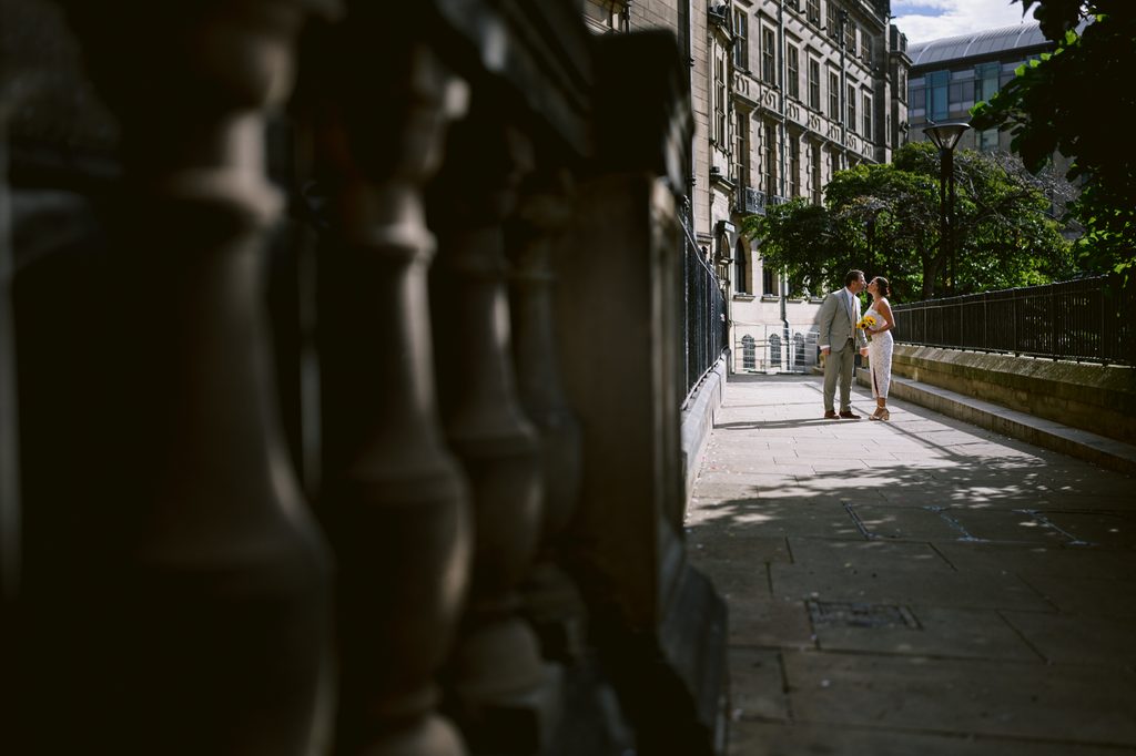 A bride and groom stand facing each other on a paved path next to the stone Sheffield Town Hall for their intimate wedding.