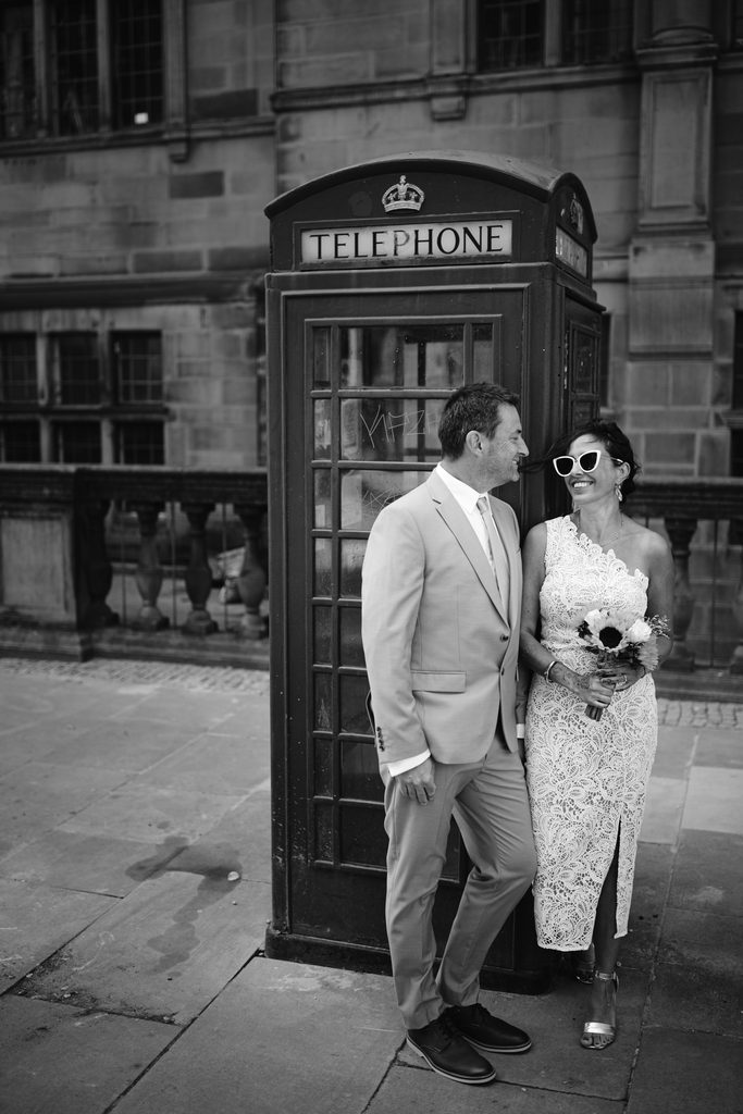 A bride and groom smile next to a traditional British telephone box during their Sheffield Town Hall wedding.