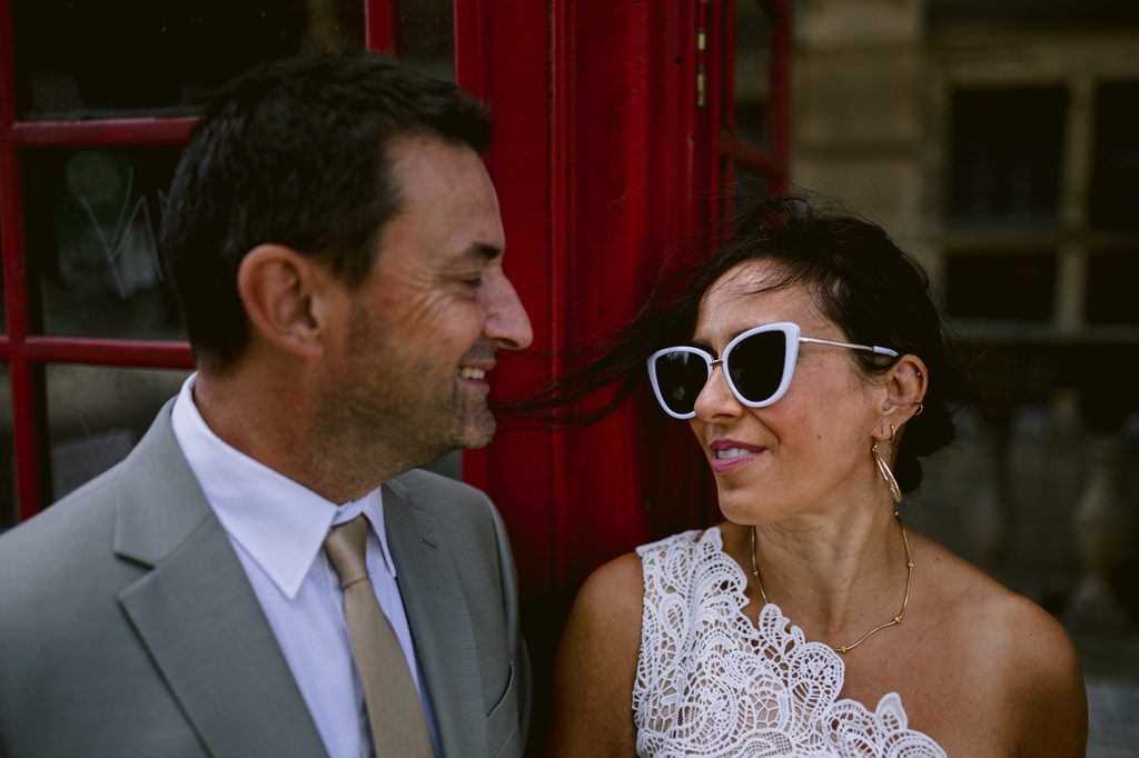 A man in a suit and a woman in a white lace top stand in front of a red telephone box during a Sheffield Town Hall wedding.